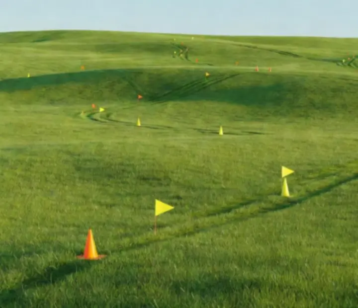 A huge open field with visible curved mowing tracks and scattered objects marking progress.